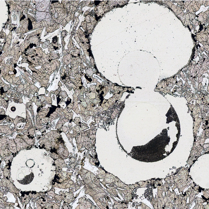 Plane-polarised image of patches of abrasive powder in air bubbles in a vesicular lava