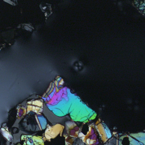 Uniaxial cross marking a dust particle in a hole in a thin section